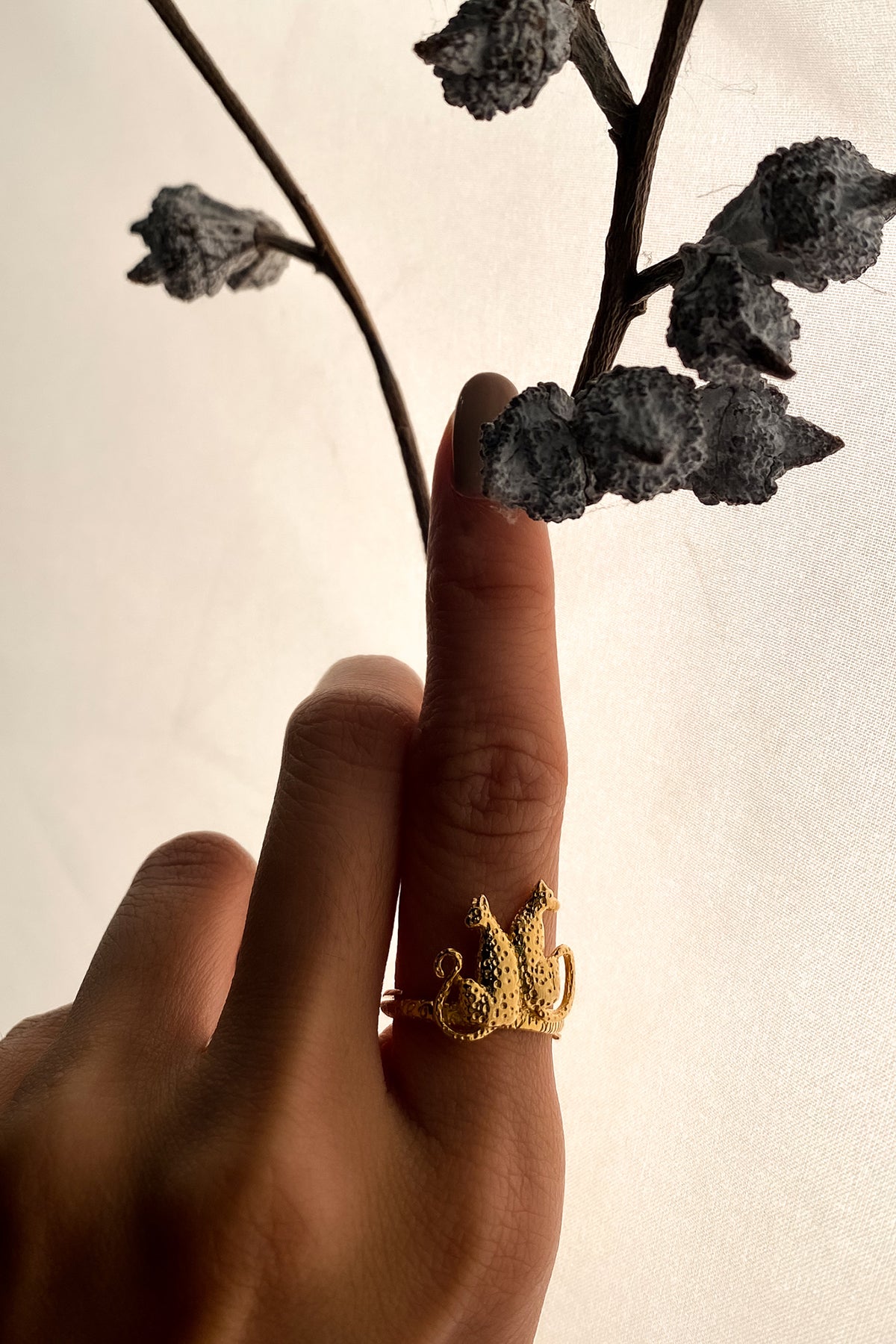 A hand with polished nails wearing a gold leopard ring against a soft, light background, highlighting the ring's intricate details.