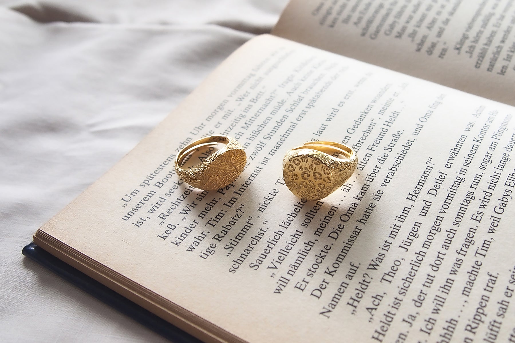 Two gold rings with distinct textures, one featuring a leopard print and the other a feather pattern placed on a book.