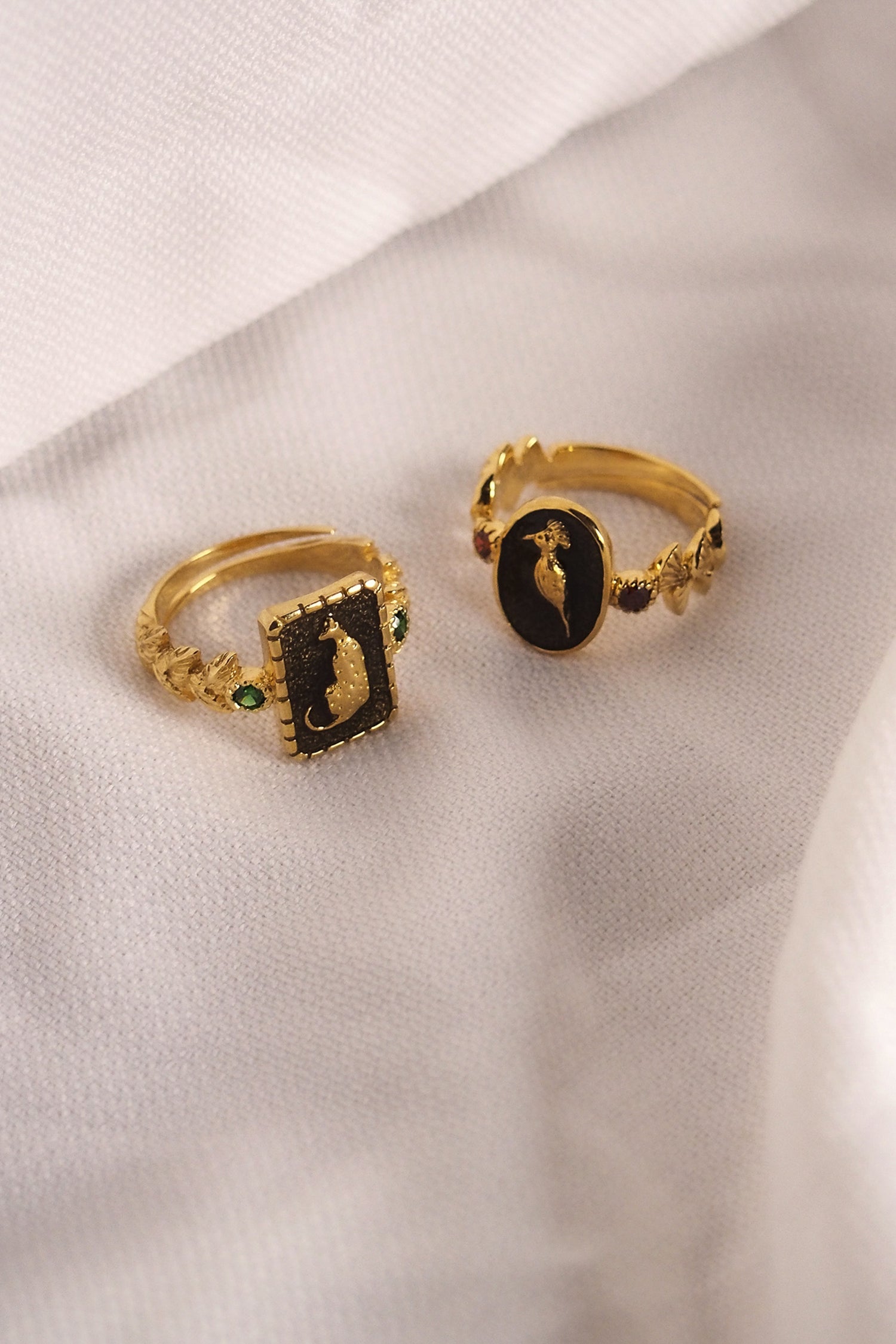 Unique golden rings with animal motifs and vibrant gemstone placed on a fabric.