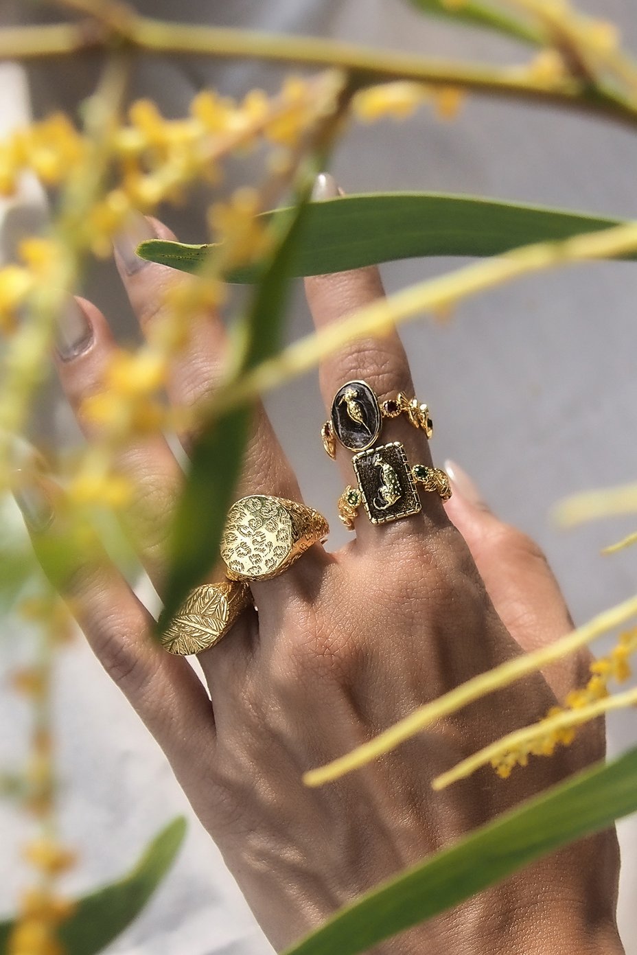 A close-up of a hand adorned with unique handcrafted golden rings, surrounded by green leaves.