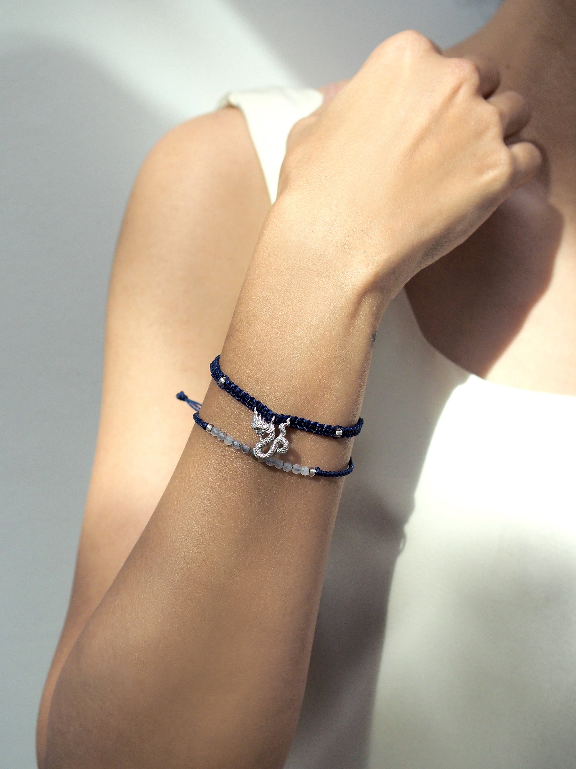 A close up of a set of two navy blue bracelets: one with a silver Naga charm, the other with grey quartz-faced beads on a person's wrist.