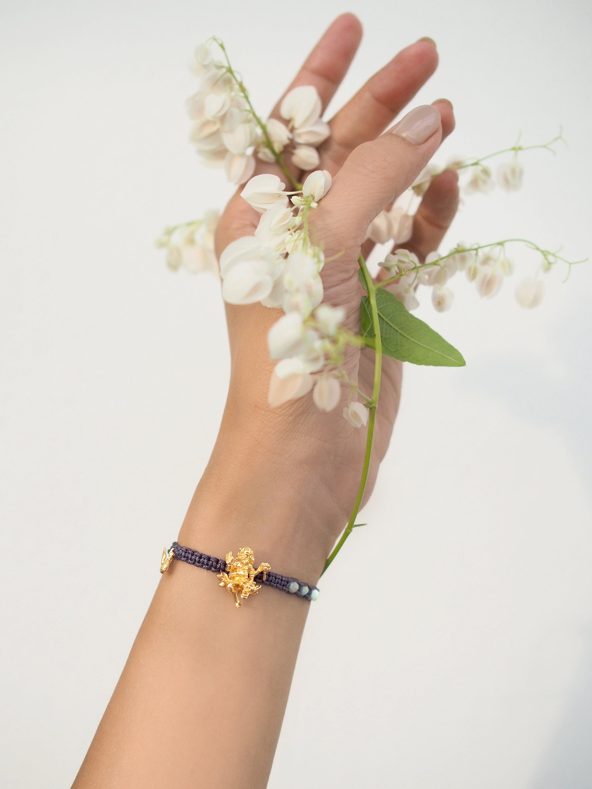 A hand with a Trimurti Brahma charm bracelet holds white flowers.