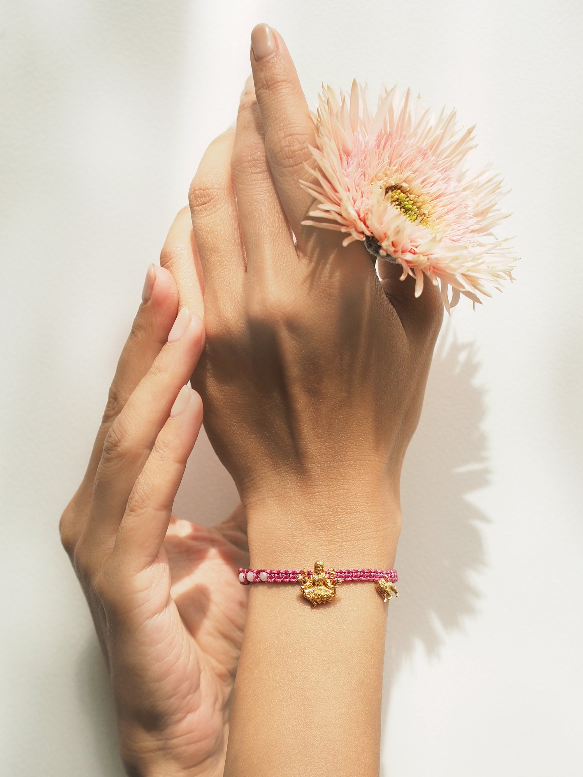 A hand with a beautiful Tridevi Parvati charm bracelet, holding a pink flower.