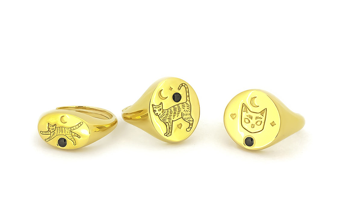 Three gold rings featuring engraved cat designs with black gemstones and moon motifs.