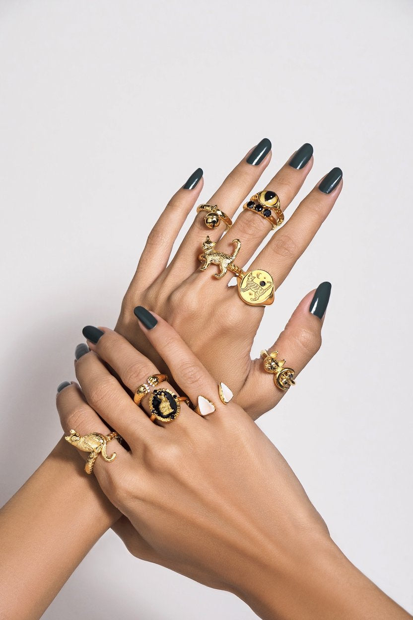 A close-up of two hands overlapping, showcasing multiple gold rings with various designs, including a cat, a moon, and a black stone.