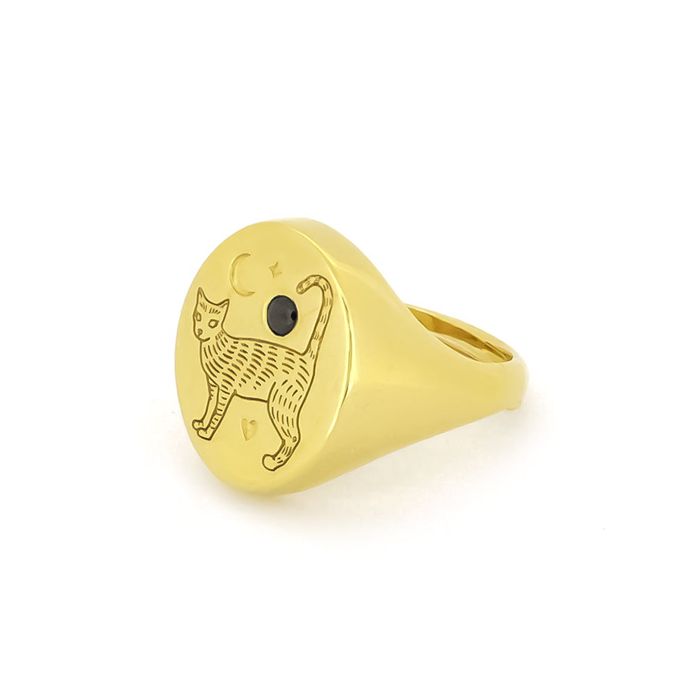 Unique gold oval-shaped ring featuring an engraved cat design and a crescent moon, complemented by a small black gemstone.