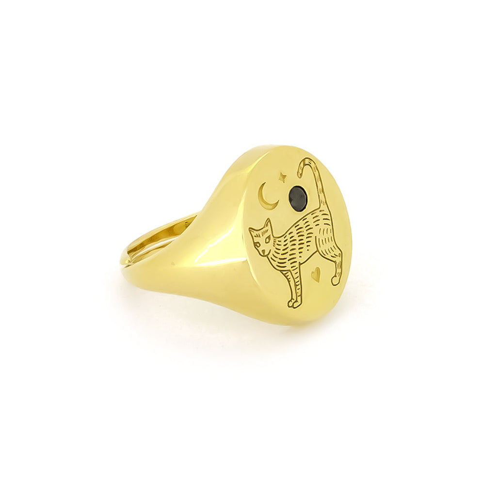 Unique gold oval-shaped ring featuring an engraved cat design and a crescent moon, complemented by a small black gemstone.