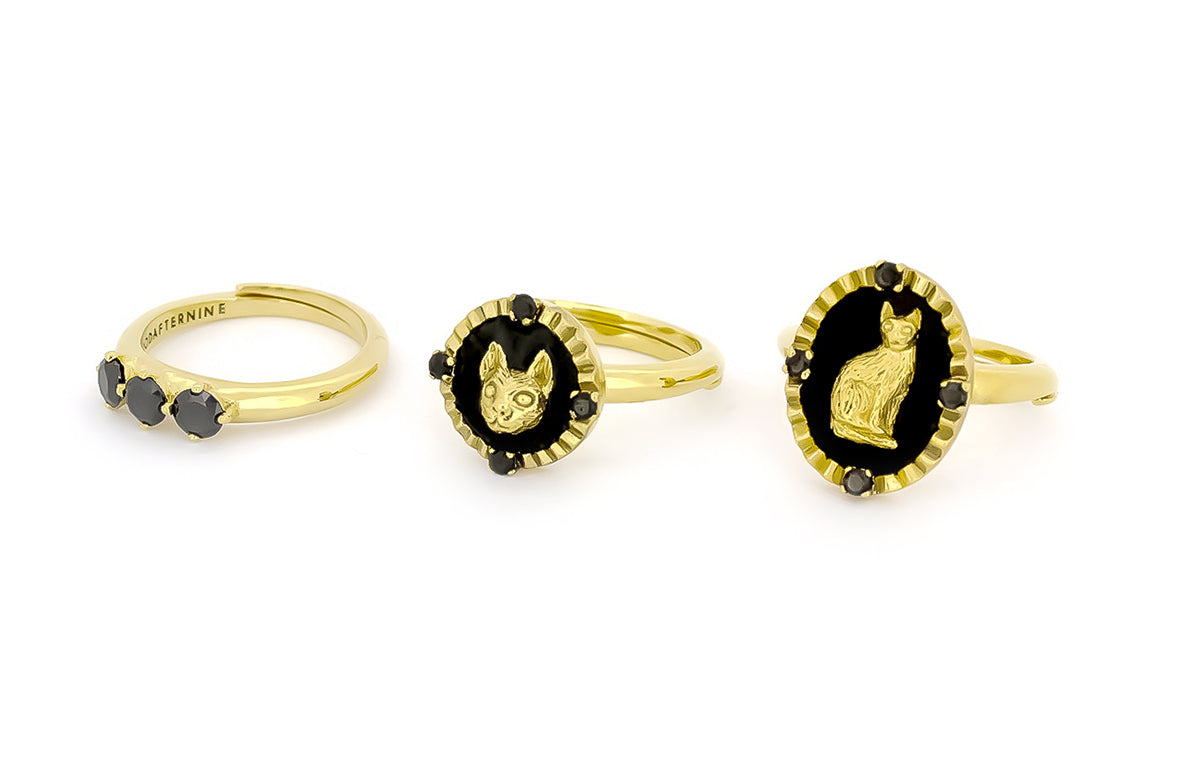 Three gold rings featuring black stones and cat designs.