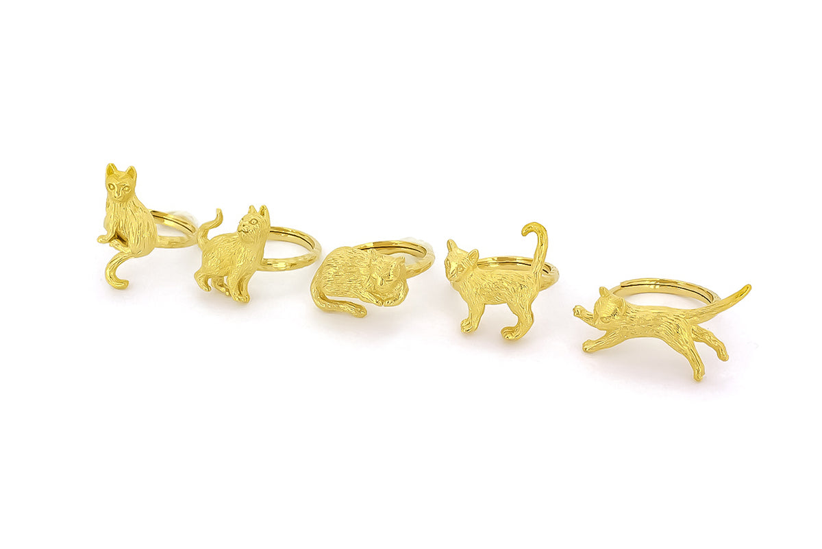 A collection of gold rings featuring playful cat designs in various poses, showcasing intricate detailing in its fur and features.