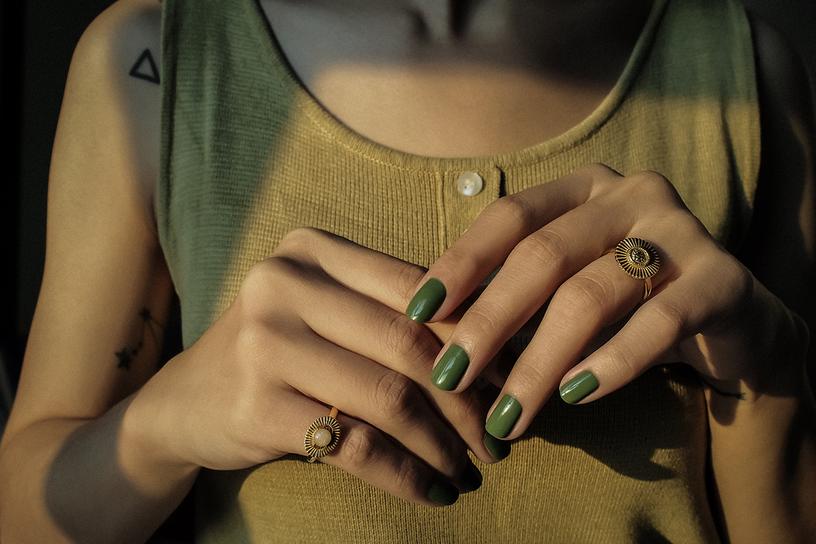 Hands with green nail polish wearing unique moon-inspired rings, displayed against a softly lit background.